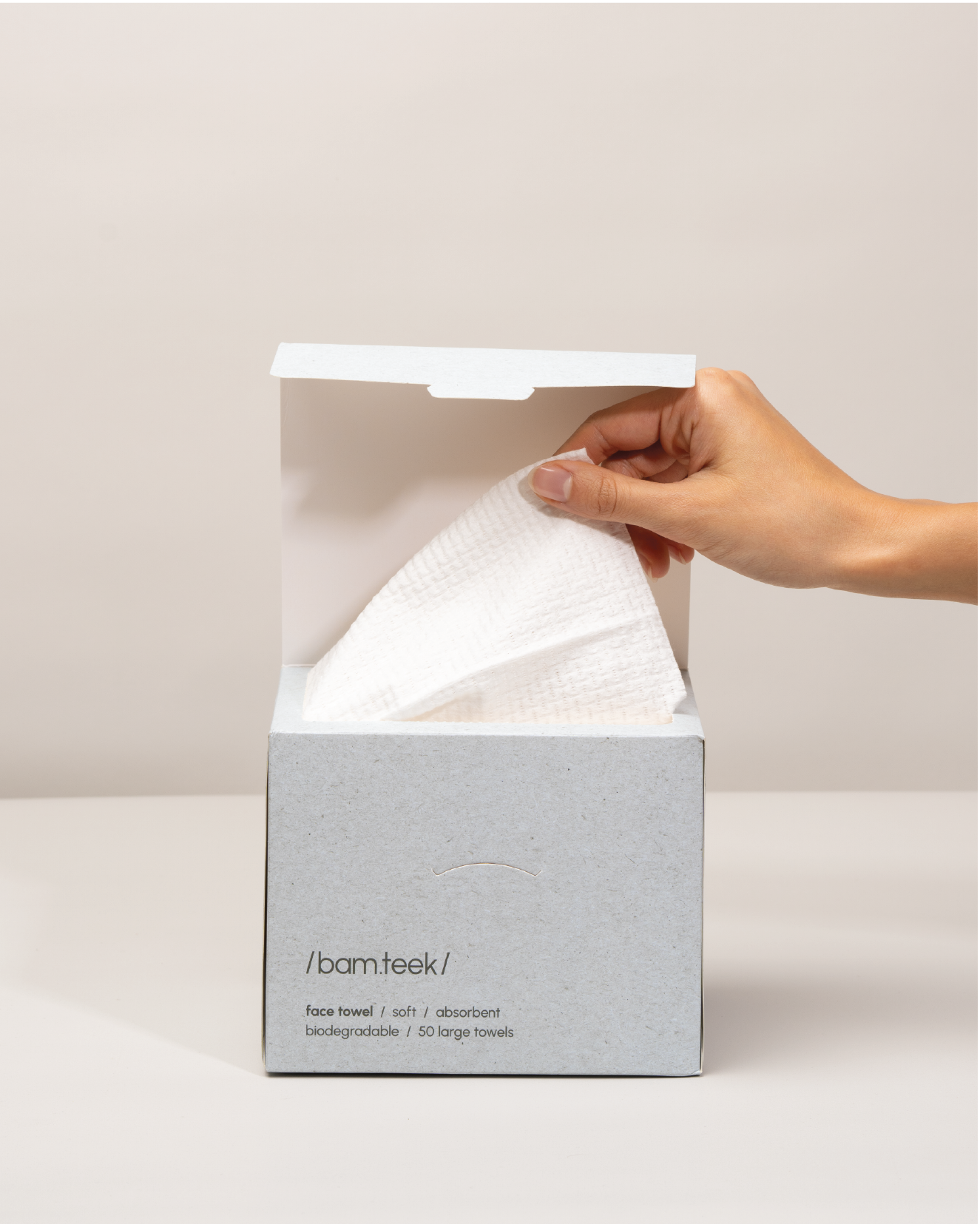 Hand reaching into Bamteek box to pull out a single-use face towel for skincare.